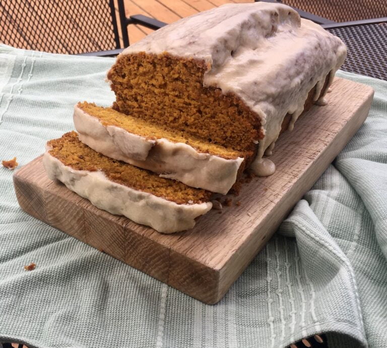 vegan pumpkin loaf with maple glaze on a wooden cutting board.