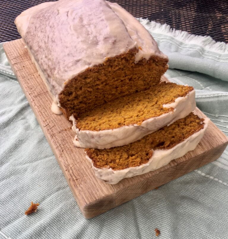 vegan pumpkin loaf with maple glaze on a wooden cutting board.