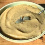 vegan potato leek soup in a green bowl with sage on top.