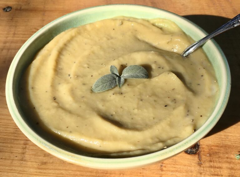 vegan potato leek soup in a green bowl with sage on top.