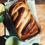 Vegan lemon babka in loaf pan with lemon simple syrup and lemons on the sides.