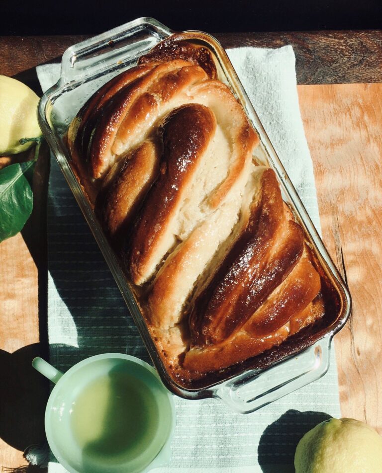 Vegan lemon babka in loaf pan with lemon simple syrup and lemons on the sides.