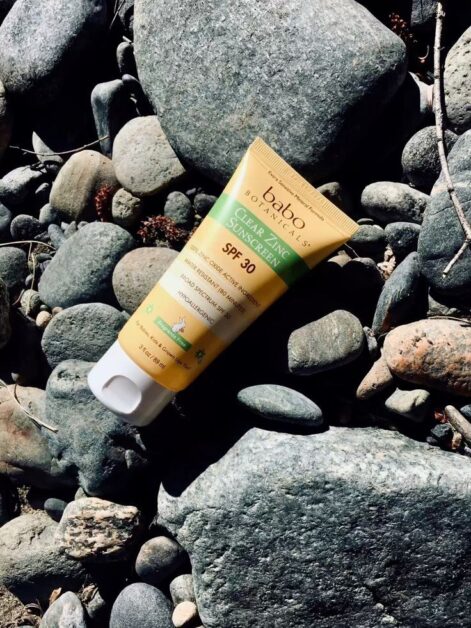 Shown is a sunscreen from Babo Botanicals sitting on river rocks, in this post are ideas for reef-safe and sustainable sunscreens are in this post.