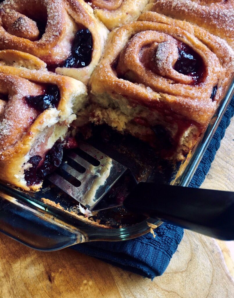 Vegan sweet rolls filled with a spiced cherry compote in a glass baking dish with a spatula.