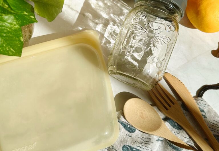 Pictured are a glass jar, silicone bag, and wooden utensils. Reusable items are ways you can reduce overconsumption.